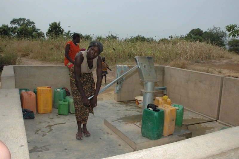 Femme utilisant un forage en brousse pour remplir des bidons